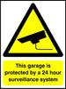 This garage is protected by a 24 hour surveillance system sign